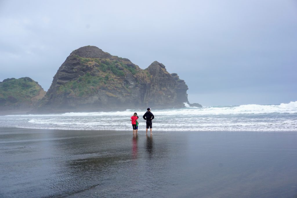Three people staring at the ocean while standing on a black sand beach.