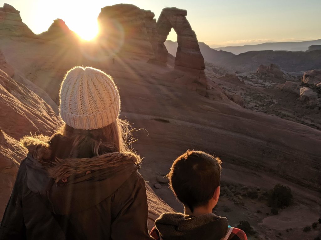 Two people looking at the delicate arch at sunrise